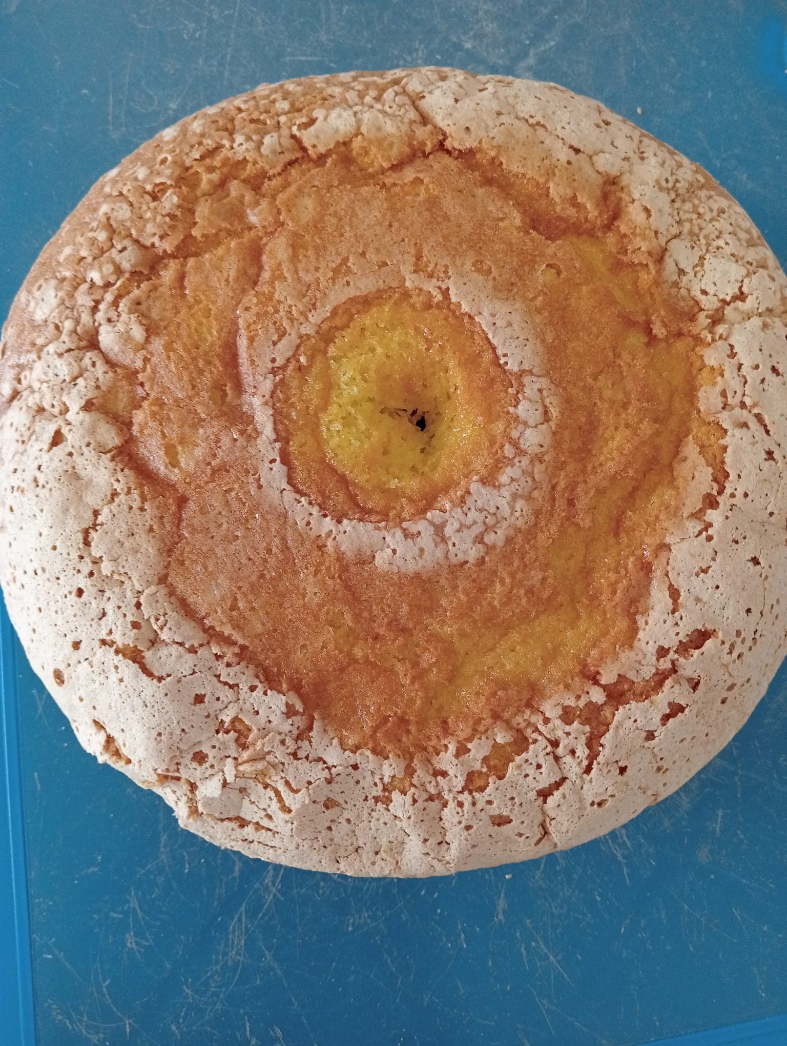 Bolo redondo dourado com crosta craquelada e açucarada sobre um fundo azul.